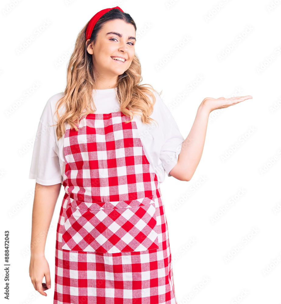 Young caucasian woman wearing apron smiling cheerful presenting and pointing with palm of hand looking at the camera. Young caucasian woman wearing apron smiling cheerful presenting and pointing with palm of hand looking at the camera.
