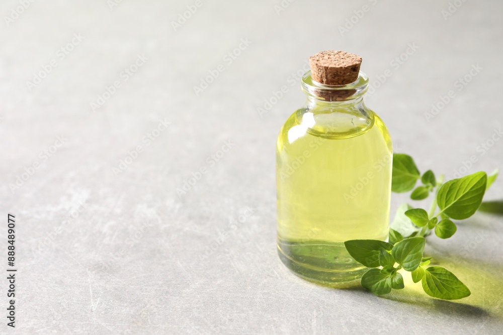 Essential oil in bottle and oregano twig on light grey textured table, closeup. Space for text Essential oil in bottle and oregano twig on light grey textured table, closeup. Space for text