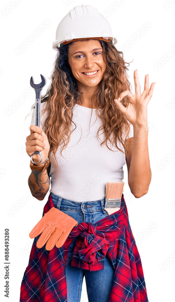 Young hispanic woman with tattoo wearing hardhat and builder clothes holding wrench doing ok sign with fingers, smiling friendly gesturing excellent symbol Young hispanic woman with tattoo wearing hardhat and builder clothes holding wrench doing ok sign with fingers, smiling friendly gesturing excellent symbol