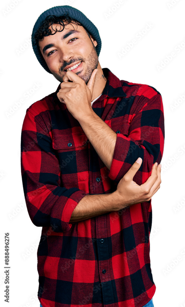 Hispanic young man with beard wearing wool winter hat smiling looking confident at the camera with crossed arms and hand on chin. thinking positive. Hispanic young man with beard wearing wool winter hat smiling looking confident at the camera with crossed arms and hand on chin. thinking positive.