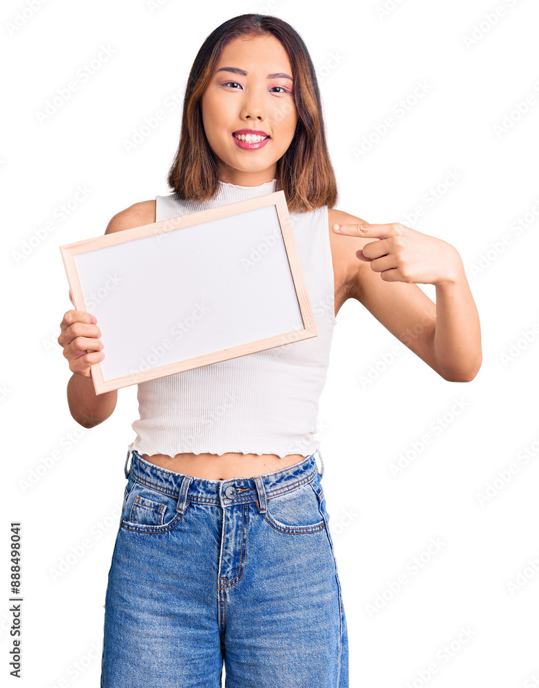 Young beautiful chinese girl holding empty white chalkboard smiling happy pointing with hand and finger Young beautiful chinese girl holding empty white chalkboard smiling happy pointing with hand and finger