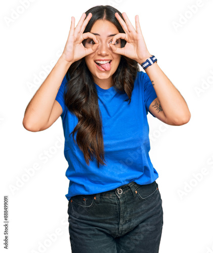 Beautiful brunette young woman wearing casual clothes doing ok gesture like binoculars sticking tongue out, eyes looking through fingers. crazy expression.