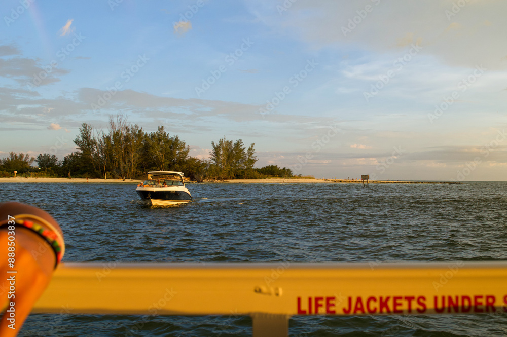Fototapeta premium Boat seen crossing the Gulf of Mexico from the point of view of another viewer on a boat. Occurring as the sun is setting. 