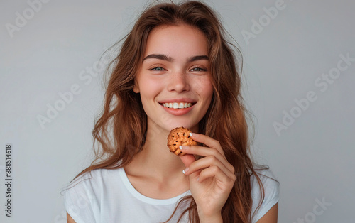 Happy young woman looking at the camera while enjoying a cookie, smiling, with a white background.