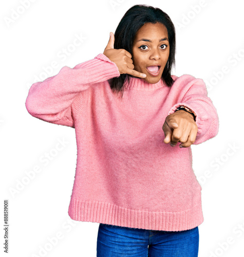 Beautiful hispanic woman wearing casual winter sweater smiling doing talking on the telephone gesture and pointing to you. call me.