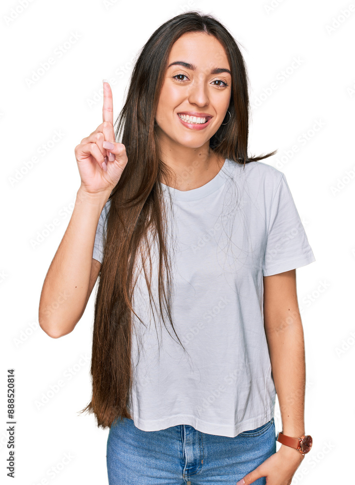 Φωτογραφία Young hispanic girl wearing casual white t shirt showing and pointing up with finger number one while smiling confident and happy