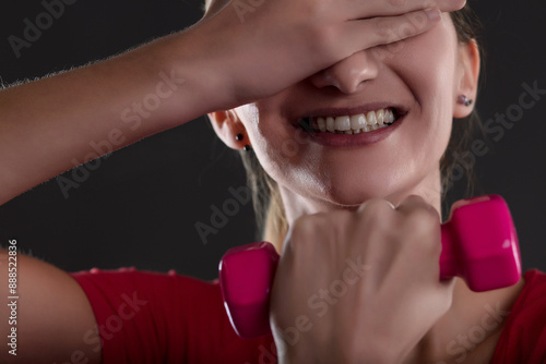 Young woman holding pink dumbbell is covering her eyes and smili photo