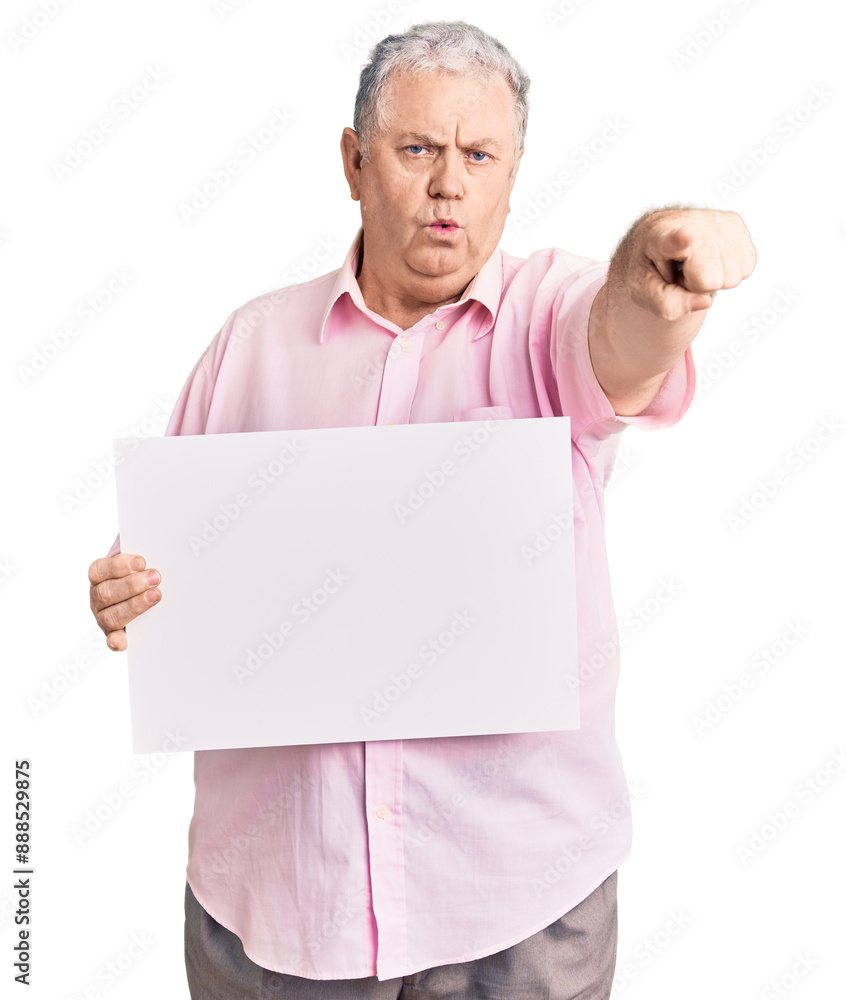Senior grey-haired man holding blank empty banner pointing with finger to the camera and to you, confident gesture looking serious Senior grey-haired man holding blank empty banner pointing with finger to the camera and to you, confident gesture looking serious