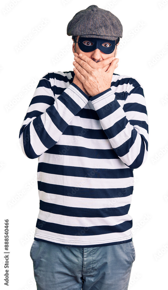 Middle age handsome man wearing burglar mask shocked covering mouth with hands for mistake. secret concept. Middle age handsome man wearing burglar mask shocked covering mouth with hands for mistake. secret concept.