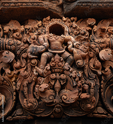 Pediment containing headless bas relief carved in red sandstone of figure without head at Banteay Srei -citadel of women and beauty- Hindu temple dedicated to god Shiva, Parvati, Siem Reap, Cambodia