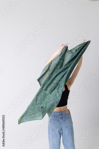 Model girl holding big green spring scarf in hands above the head and posing on white background. Woman wears blue jeans photo