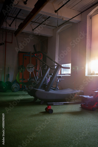 Moody portrait view of cardio equipment and lifting rack at indoor performance fitness studio.