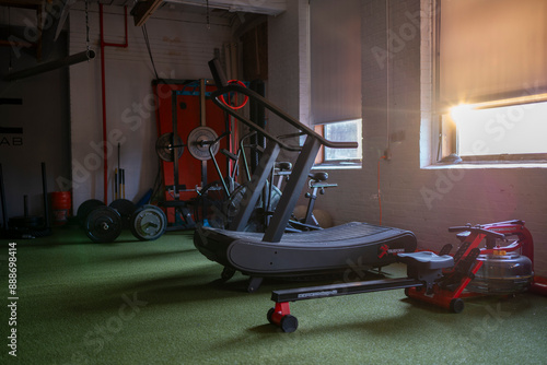 Moody landscape view of cardio equipment and lifting rack at indoor performance fitness studio.