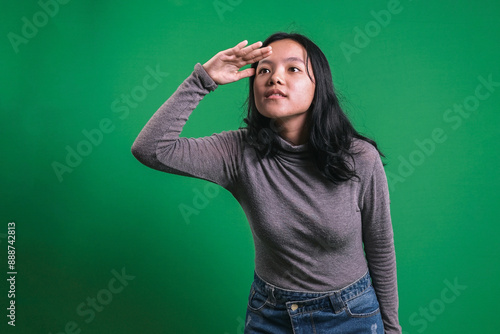 Asian Young Woman Put Hand Over Forehead And Looking Far Away on Green Background