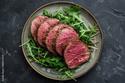 Plate with roasted beef steak and arugula on dark background top view