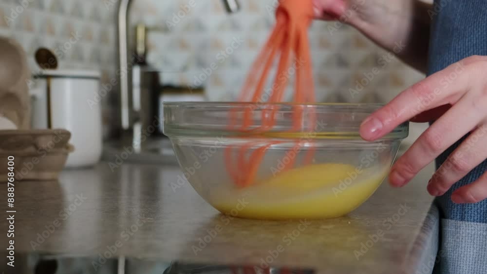 Close-up of female's hands whipping eggs with a whisk in a glass bowl while preparing breakfast in the kitchen. Home cooking concept. Close-up of female's hands whipping eggs with a whisk in a glass bowl while preparing breakfast in the kitchen. Home cooking concept.