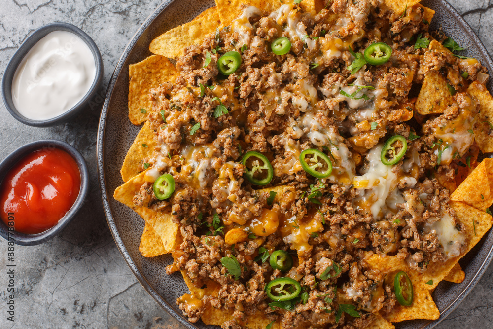 Φωτογραφία Traditional nachos with ground beef, cheddar cheese and jalapeno  pepper served with sauces closeup on the plate on the table