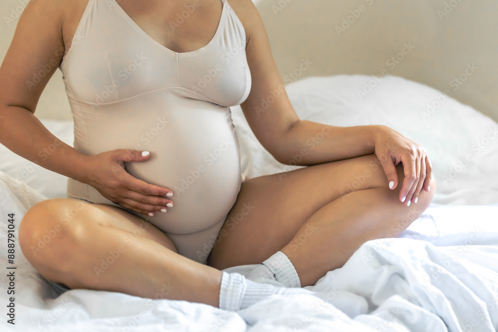 Caucasian pregnant woman touching her belly while sitting on the bed at home. Caucasian pregnant woman touching her belly while sitting on the bed at home.