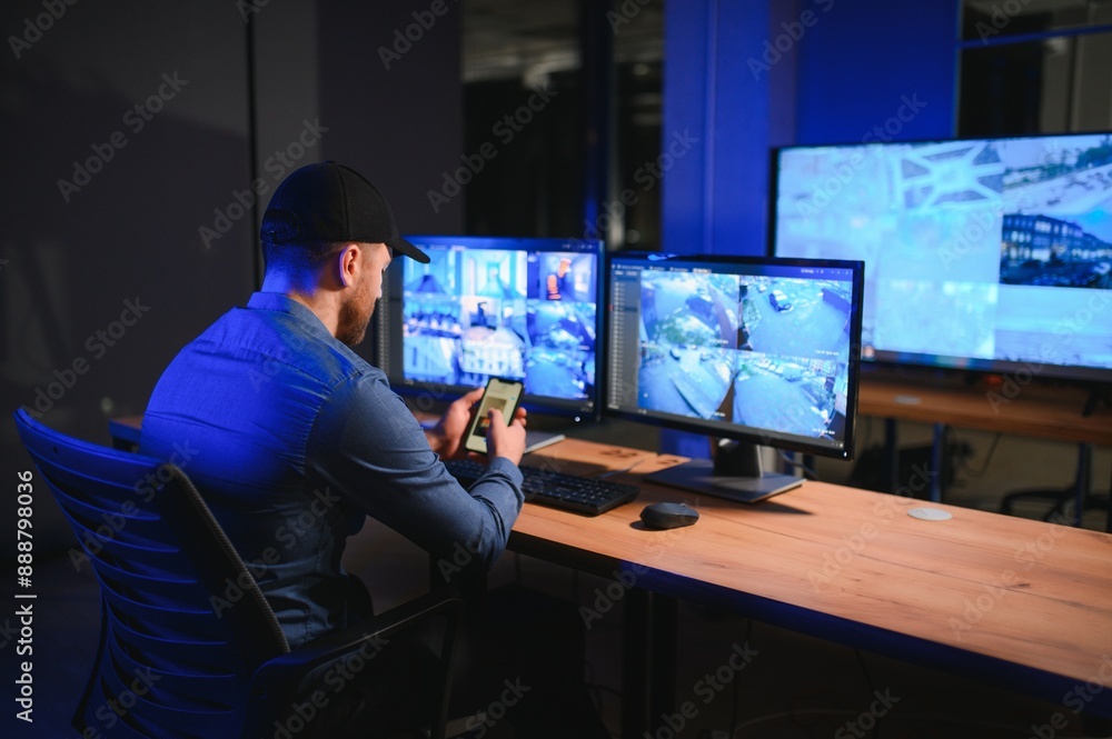 Rear view of security system operator looking at CCTV footage at desk in office Rear view of security system operator looking at CCTV footage at desk in office