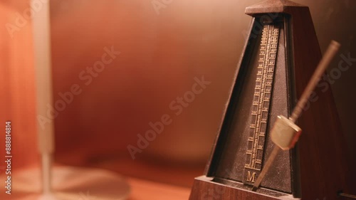 Dusty metronome that is moving back and forth on a lamp lit shelf. photo