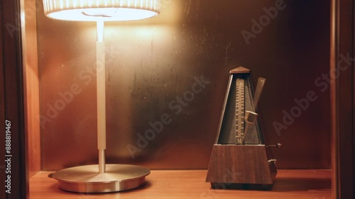 Static shot of a shelf that a metronome is sitting on and a hand comes in and sets the pendulum swinging. photo