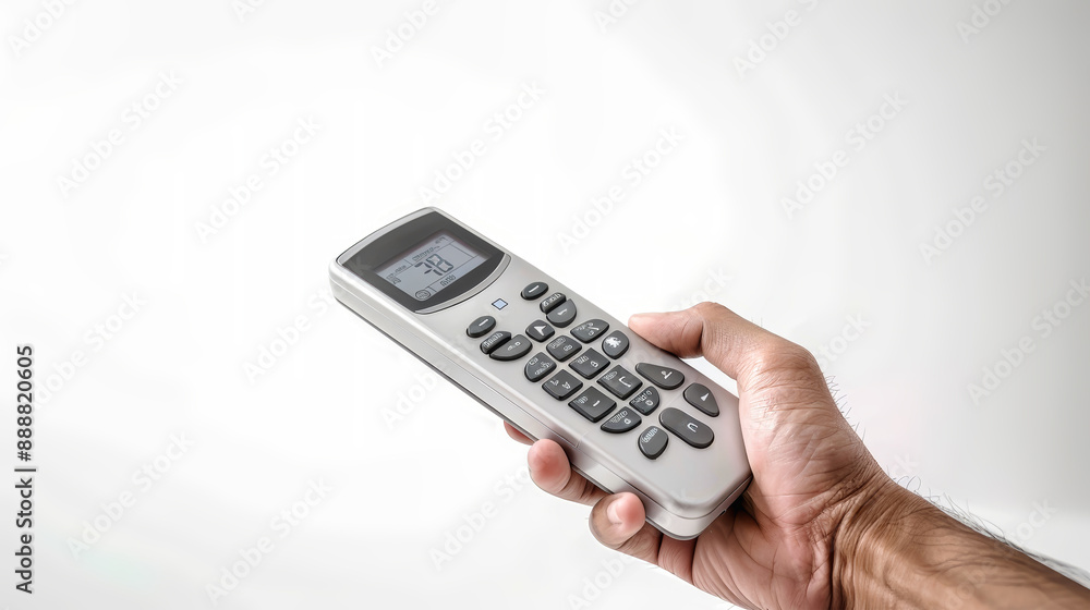 A hand holds an air conditioner remote control with a digital display and buttons, against a white backdrop A hand holds an air conditioner remote control with a digital display and buttons, against a white backdrop
