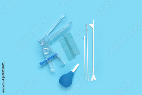 Gynecological speculum with pap smear test tools and enema on blue background