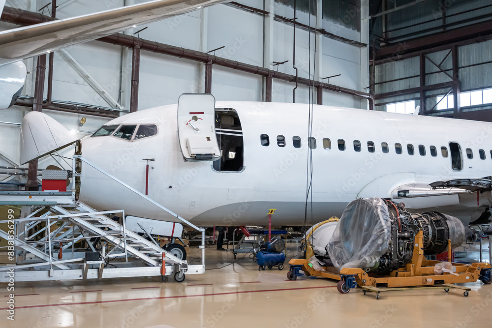 The front part of passenger airplane in aviation hangar. A removed aircraft engine is located next to the plane. Airliner under maintenance The front part of passenger airplane in aviation hangar. A removed aircraft engine is located next to the plane. Airliner under maintenance