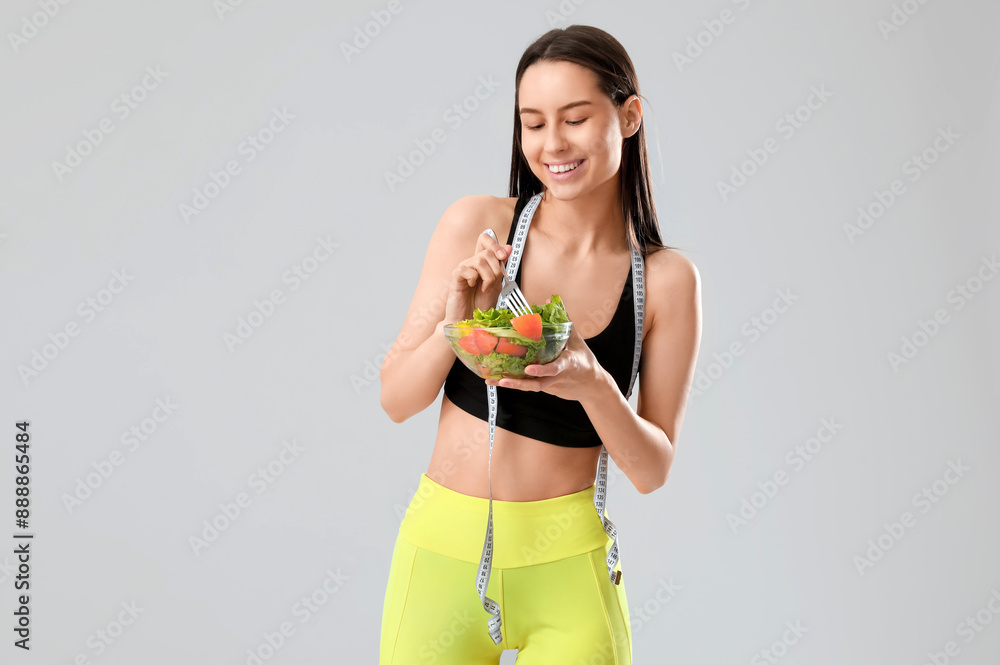 Beautiful young happy woman with measuring tape and bowl of fresh salad on grey background. Weight loss concept Beautiful young happy woman with measuring tape and bowl of fresh salad on grey background. Weight loss concept
