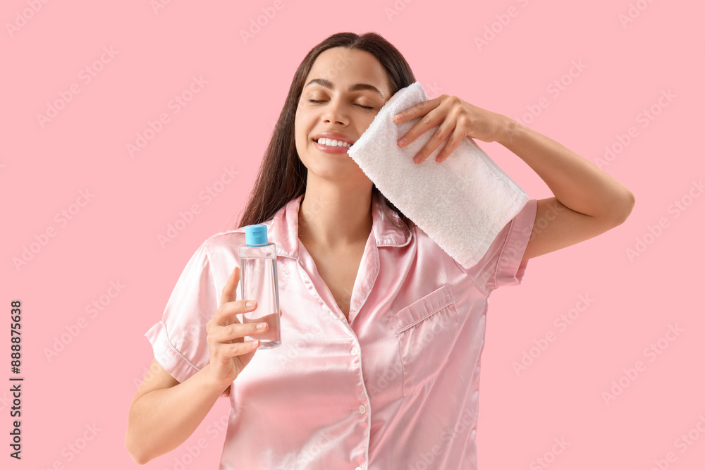 Beautiful young happy woman with towel and bottle of micellar water on pink background Beautiful young happy woman with towel and bottle of micellar water on pink background