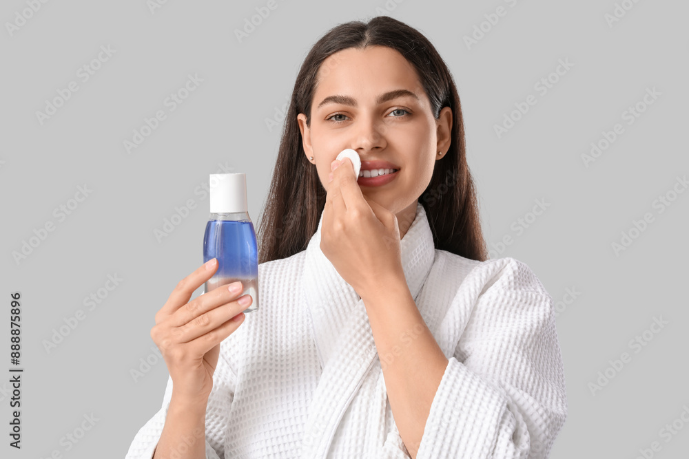 Beautiful young happy woman with cotton pad and bottle of micellar water on grey background Beautiful young happy woman with cotton pad and bottle of micellar water on grey background