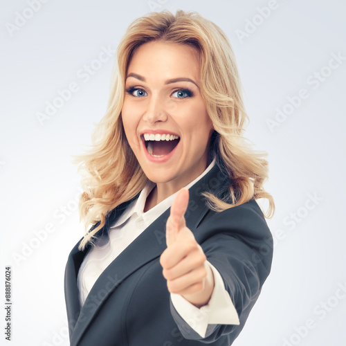 Happy smiling businesswoman in grey confident suit, showing thumbs up gesture, isolated over gray background. Business success concept. Copy space for some text.