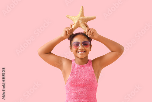 Happy African-American girl with starfish on pink background
