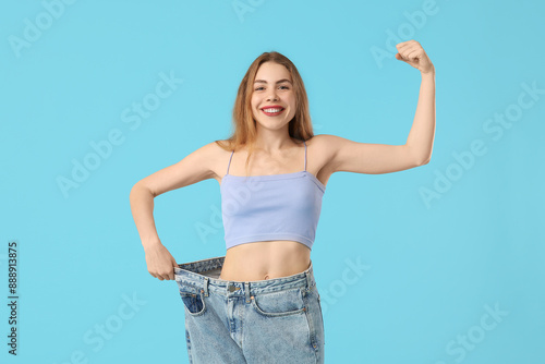 Young woman in loose jeans on blue background. Diet concept