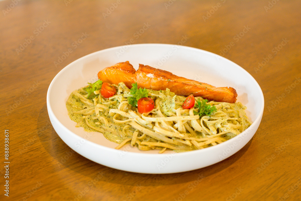 Italian food concept. Pesto pasta with salmon grilled in a white dish on a wooden table. Italian food concept. Pesto pasta with salmon grilled in a white dish on a wooden table.