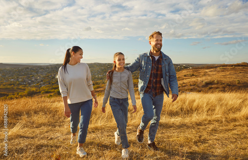 Fotografie Happy smiling young family with child girl walking in the field enjoying nature at sunset