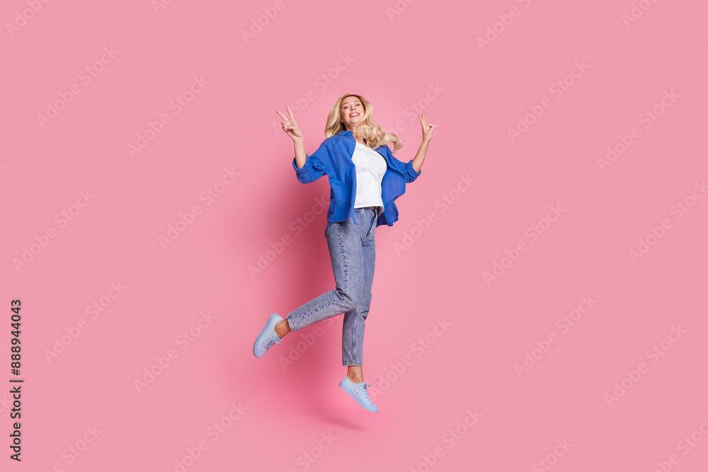 Full size photo of cheerful woman dressed blue shirt denim trousers flying showing v-sign symbol isolated on pink color background Full size photo of cheerful woman dressed blue shirt denim trousers flying showing v-sign symbol isolated on pink color background