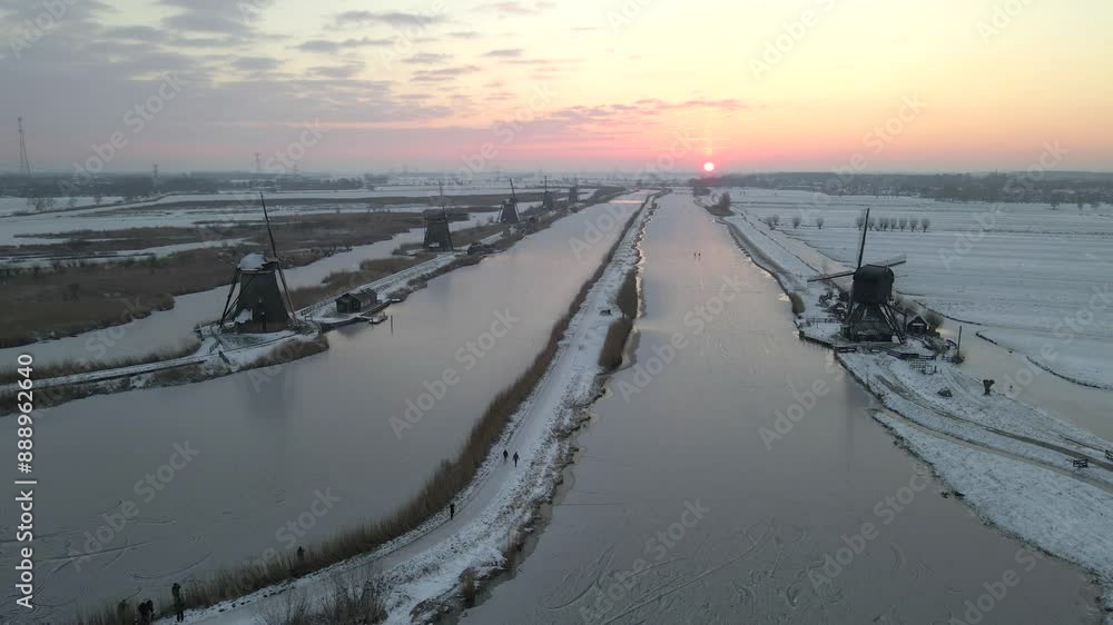 Aerial view of snow-covered windmills along a frozen river at sunrise, Kinderdijk, Netherlands. Aerial view of snow-covered windmills along a frozen river at sunrise, Kinderdijk, Netherlands.