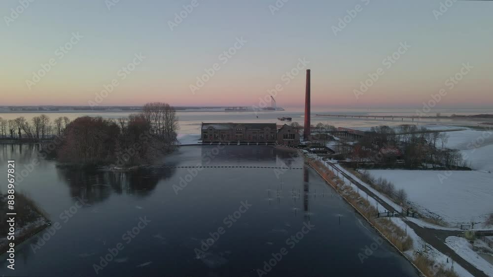 Aerial view of snowy pumping station and chimney by the lake, Lemmer, Friesland, Netherlands. Aerial view of snowy pumping station and chimney by the lake, Lemmer, Friesland, Netherlands.