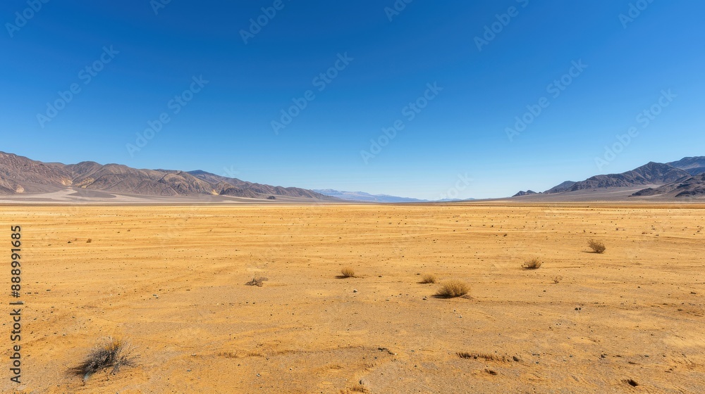 Fototapeta premium A desert landscape with a clear blue sky. The sky is dotted with clouds, and the sun is shining brightly. The emptiness of the desert gives a sense of solitude and vastness