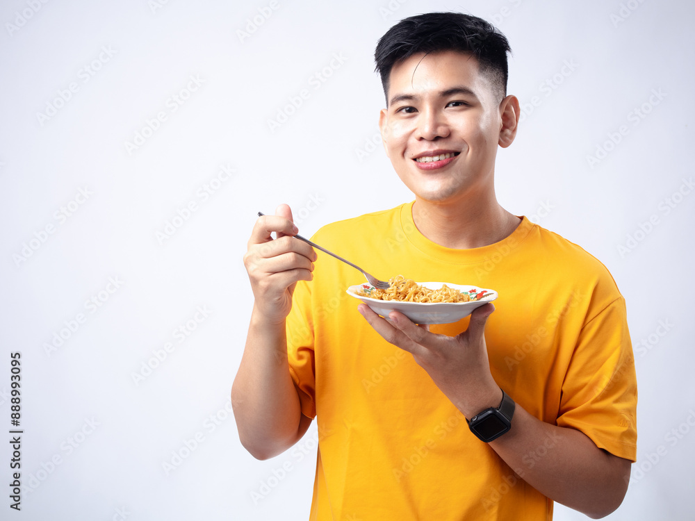 Chinese Indonesian man in yellow shirt picking up fried noodles with fork from a white plate, while smiling and closing his eyes. Isolated in white background. Chinese Indonesian man in yellow shirt picking up fried noodles with fork from a white plate, while smiling and closing his eyes. Isolated in white background.