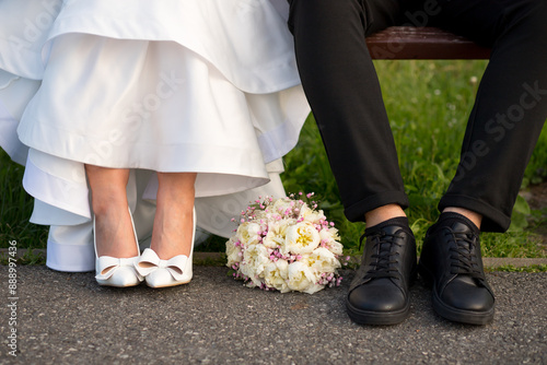 The bride's foot in a tube and Denise's black sneakers, the bride's bouquet lies on the ground next to the shoes of the bride and groom. Wedding day details. Wedding photo shoot