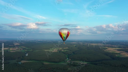 Aerial view tracking shot of a hot air balloon above a beautiful german vilige filled with green trees during sunset and golden hour photo