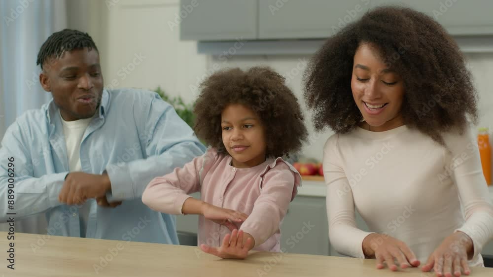 Happy funny smiling African American family parents man father male husband woman female mother dancing together fooling fun at table kitchen dance little child kid girl daughter listening music joy