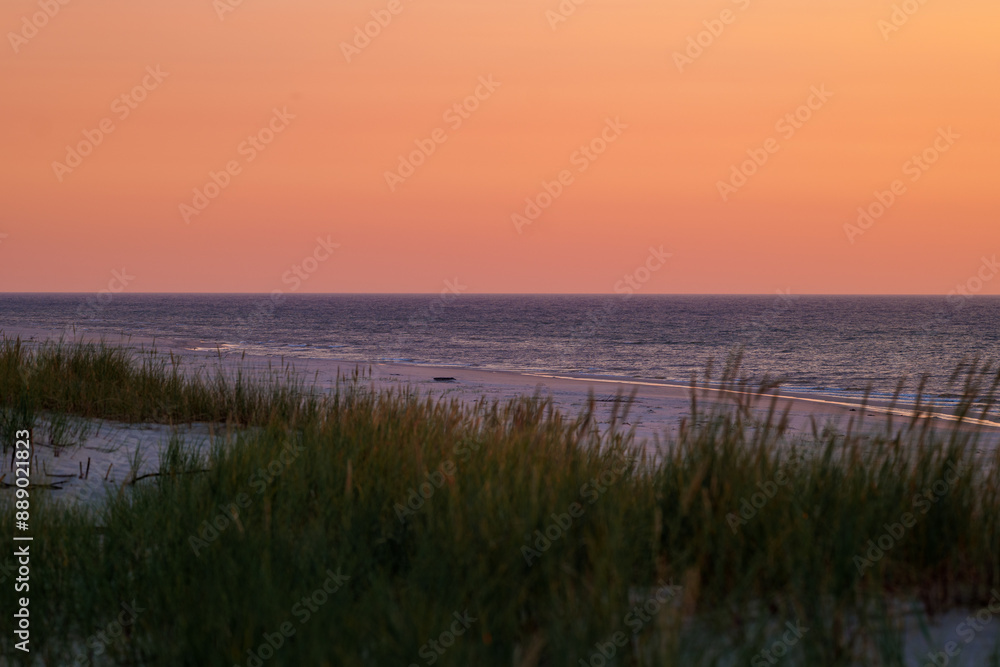 Beautiful orange sky over the sea. Blurry grass in the foreground. Beautiful sandy beach. Golden hour. Baltic Sea, Slajszewo, Poland Beautiful orange sky over the sea. Blurry grass in the foreground. Beautiful sandy beach. Golden hour. Baltic Sea, Slajszewo, Poland