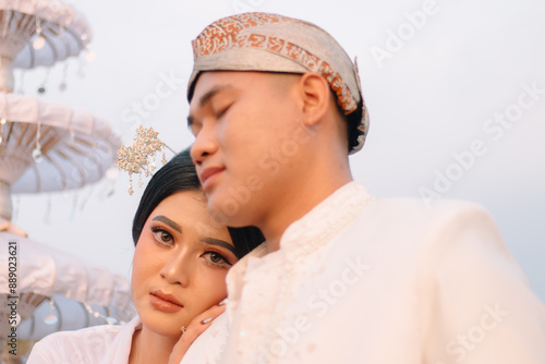 A pair of young Asian boy and girl lovers standing, the man sleeping on the woman's shoulders wearing modern Javanese traditional clothing, the bride's white velvet kebaya. beauty, fashion photo