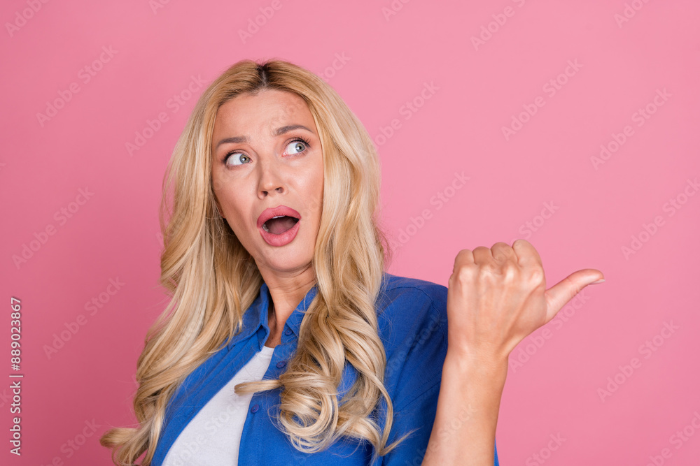 Photo of charming impressed woman wear blue shirt looking pointing thumb back empty space isolated pink color background