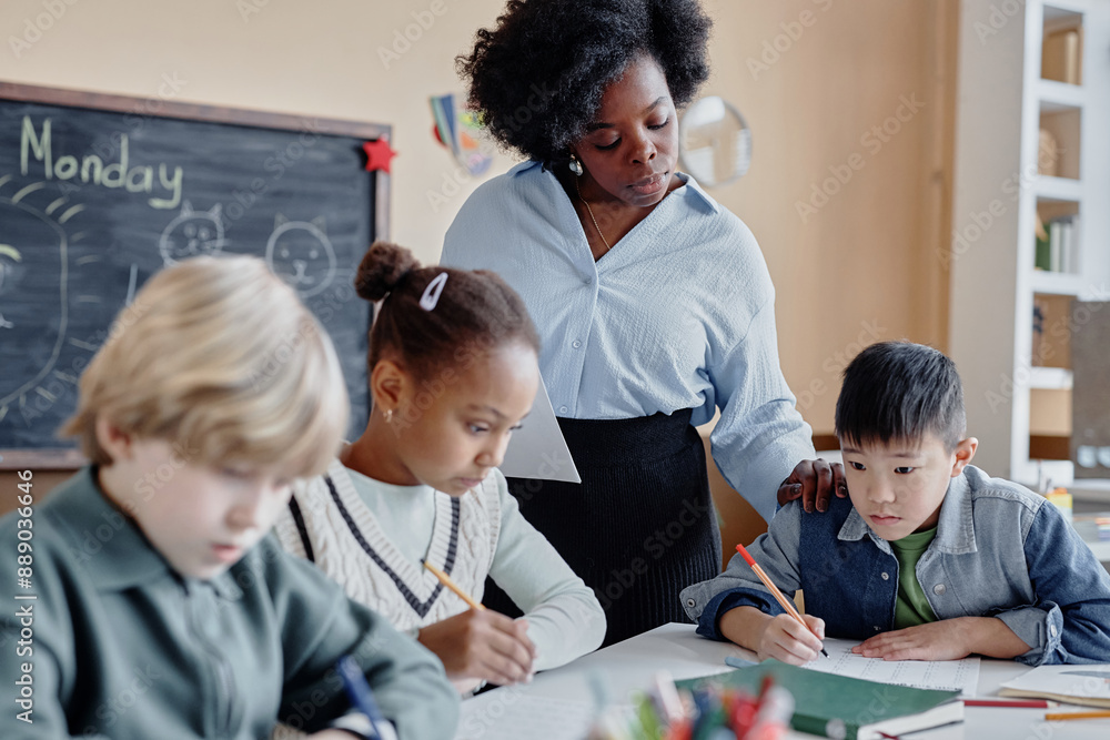 © Seventyfour - Shot of female teacher of Black ethnicity supervising multiethnic young students writing test or solving examples in classroom © Seventyfour - Shot of female teacher of Black ethnicity supervising multiethnic young students writing test or solving examples in classroom