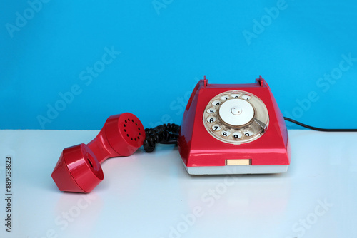 Old red retro telephone with the receiver raised on a blue background.