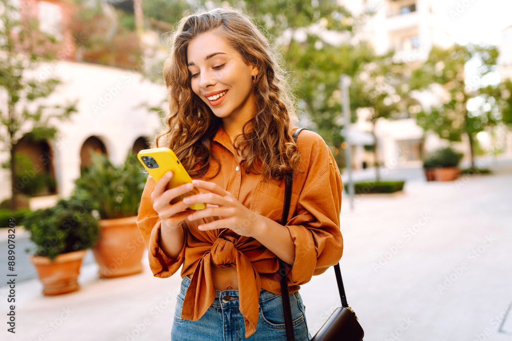 Young woman using a smart phone while walking on a sidewalk in the city. Business, technology, blogging, communication concept. Young woman using a smart phone while walking on a sidewalk in the city. Business, technology, blogging, communication concept.